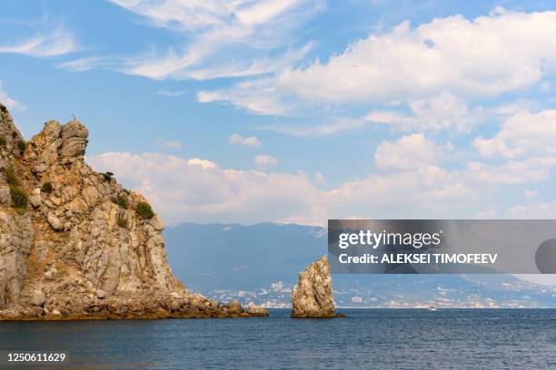 the sheer shore of a stone mountain in the black sea with a motor ship on the horizon, on a bright sunny day with clouds in the sky. - krim stockfoto's en -beelden