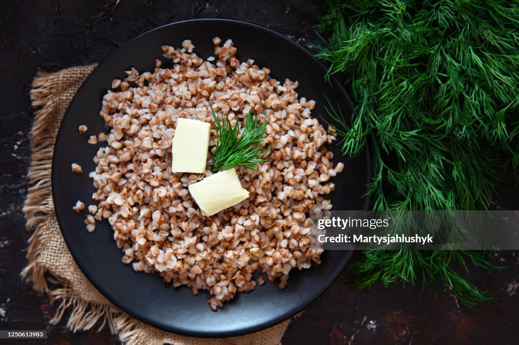 Freshly cooked buckwheat porridge with pieces of butter and with green dill on a dark background. Healthy food.