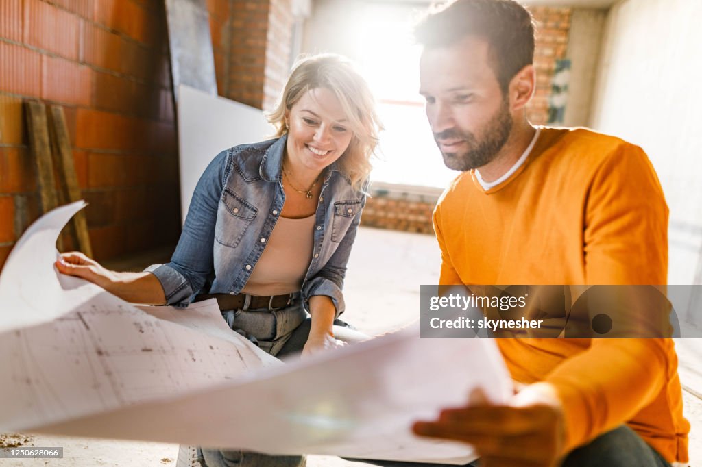 Happy couple analyzing plans at their renovating apartment.