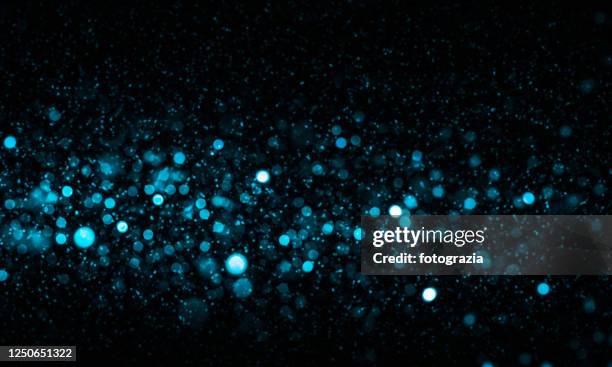 defocused lights and dust particles over black background - blue glitter fotografías e imágenes de stock