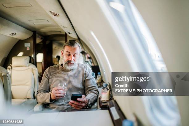 ceo de la compañía usando un teléfono inteligente y bebiendo vino mientras viaja a bordo de un jet privado - first class fotografías e imágenes de stock