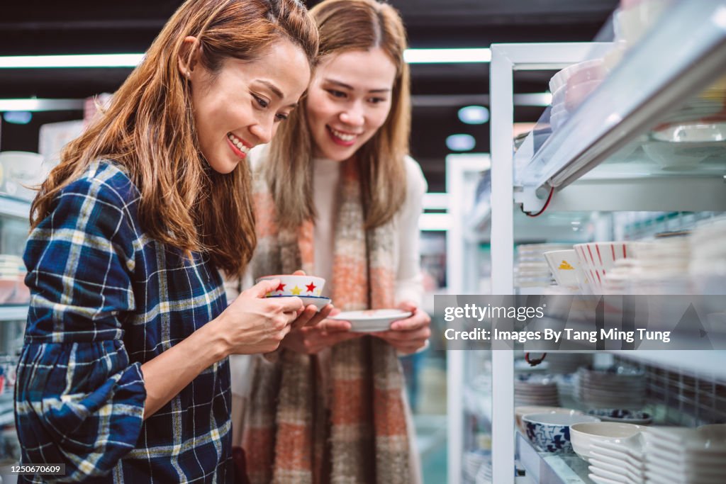 Portriat of young cheerful girlfriends shopping for ceramic tablewares in department store joyfully