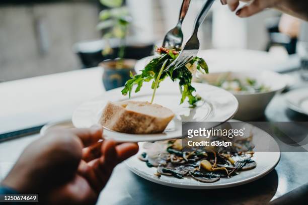 cropped shot of a couple serving healthy salad on plate and sharing food while having lunch in a restaurant - couple fine dining stock pictures, royalty-free photos & images