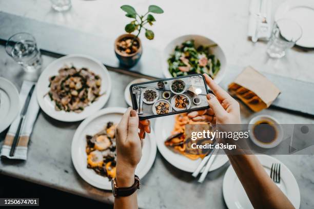 overhead view of a woman's hand taking photo of freshly served food before eating it with smartphone in a restaurant - foodie stockfoto's en -beelden