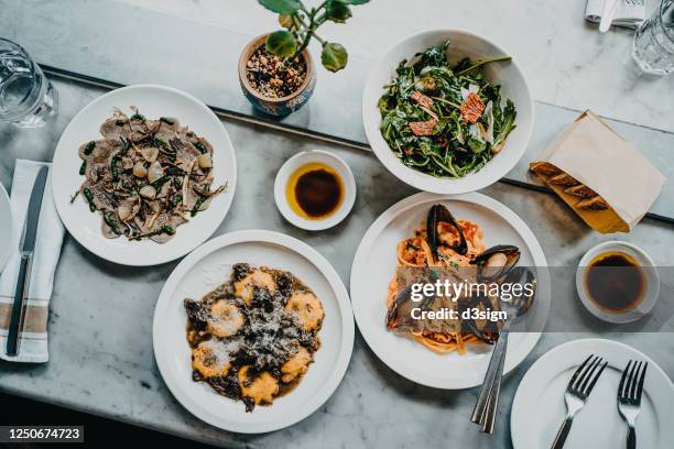 flat lay of meal for two people with fresh green salad, appetizer, seafood linguine and beef ravioli freshly served on dining table in a restaurant - 豪華　食事 ストックフォトと画像