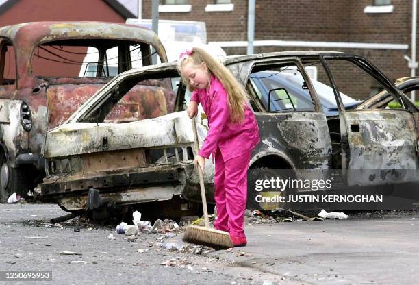 Surrounded by burnt out vehicles, a young girl still in her pyjamas attempts to clean the footpath outside her house on Ardoyne Road, Belfast, 13...