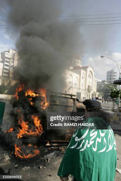 An Islamist protester, draped with a green banner with Islamic calligraphy, looks at a car set on fire 05 February 2006 in Beirut in the latest...