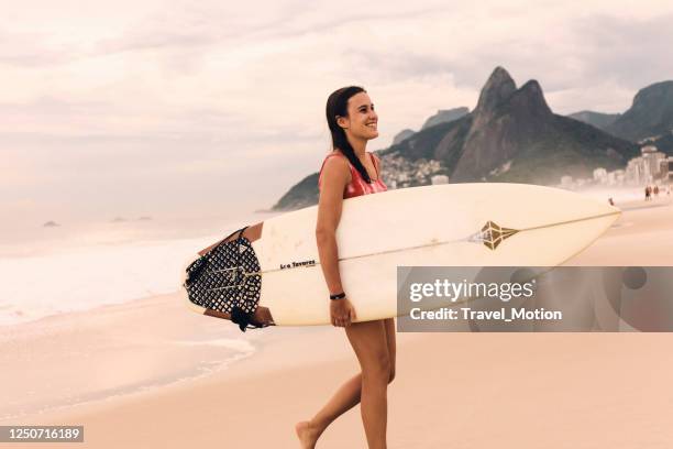 young woman carrying surfboard at ipanema beach - ipanema beach stock pictures, royalty-free photos & images