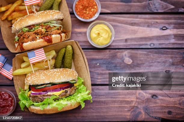 food served at a picnic table for july 4th celebration.on the table are traditionally grilled dishes american hamburgers, pulled pork, french fries and condiments - burger with flag stock pictures, royalty-free photos & images