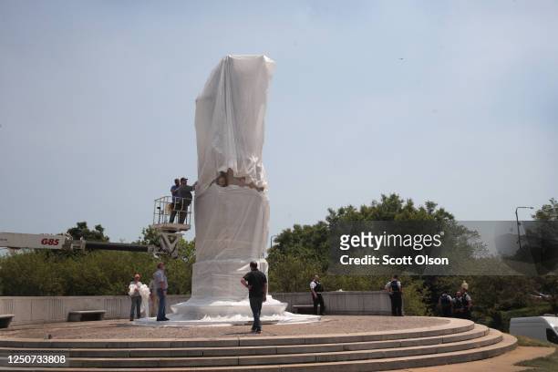 Workers cover a statue of Christopher Columbus before the start of a Juneteenth march organized by faith leaders on June 19, 2020 in Chicago,...