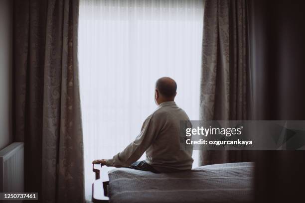 älterer mann sitzt auf dem bett und sieht ernst aus - lonely stock-fotos und bilder