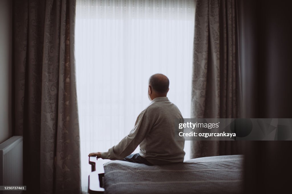 Elderly man sitting on bed looking serious