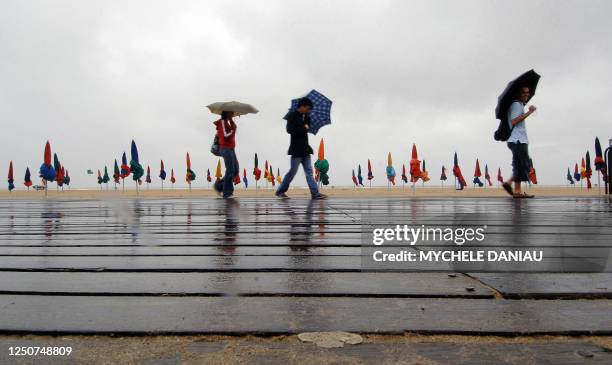 People walk on the boardwalk at the beach 19 August 2007 in Deauville, northwestern France. Tourist activities in France, obscured by grey skies and...