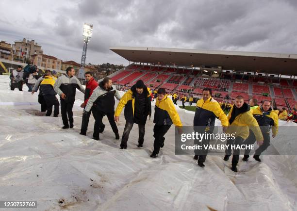 People remove a protection against the rain on the field of the Ray Stadium in Nice, southern France, on December 14, 2008 before the French L1...