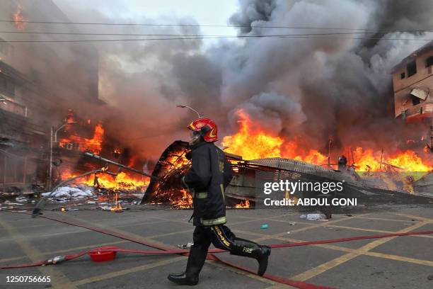 Firefighter runs to extinguish a fire that broke out in a clothing market in Dhaka on April 4, 2023. - Hundreds of firefighters were battling an...