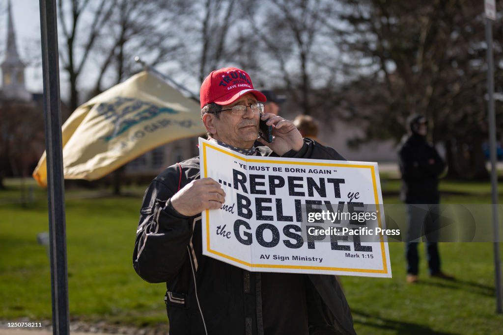 A man with a religious sign and wearing a Trump hat protests...