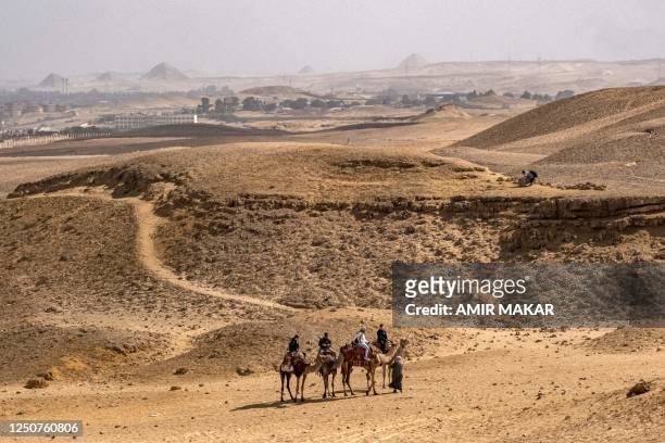 In this picture taken on February 6 camel guides lead tourists riding at the Giza necropolis, with the Step Pyramid of Saqqara and other features at...
