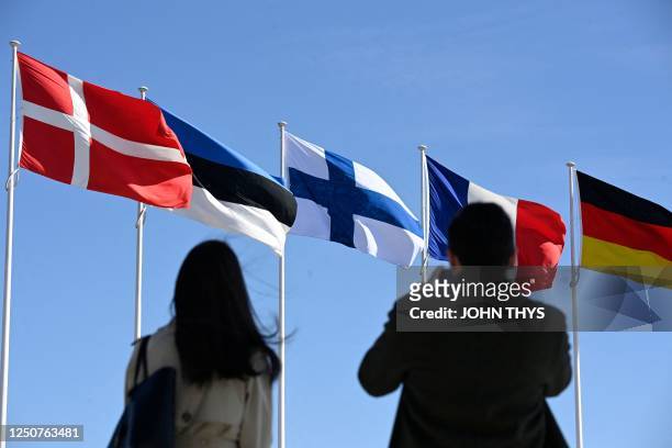People stand in front of the Finnish national flag after a flag-raising ceremony at the NATO headquarters in Brussels, on April 4, 2023. - Finland on...