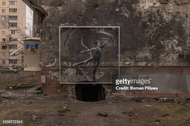 Graffiti under a protective screen created by British artist Banksy showing a woman in a leotard and a neck brace waving a ribbon on the wall of a...