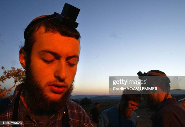 Israeli settlers pray early 10 June 2003 next to caravans, as they prepare for a possible evacuation of their illegal outpost, by the name of Gilad...