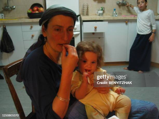 Bracha Benyitzhak, mère de 14 enfants, tient sur ses genoux, dans sa cuisine, Alhinoa, 2 ans, le dernier né de la famille, sous le regard de Hana ....