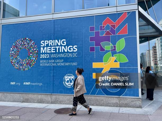 Woman walks past a sign for the 2023 Spring Meetings of the World Bank/International Monetary Fund on the IMF building in Washington, DC, on April 5,...