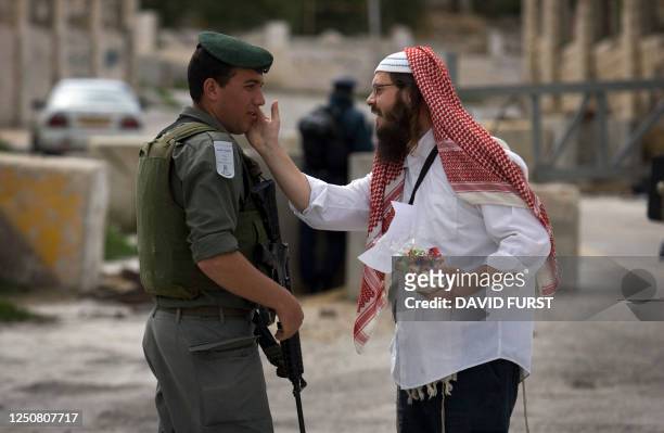 Jewish settler dressed in an Arab headscarf gestures to an Israeli soldier standing guard for a parade in celebration of the Jewish holiday of Purim...