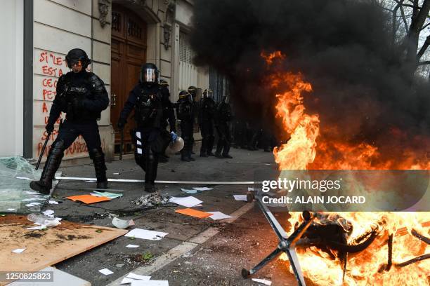 French CRS riot police run past a vandalized bank, and office furniture set ablaze on the street during a demonstration on the 11th day of action...