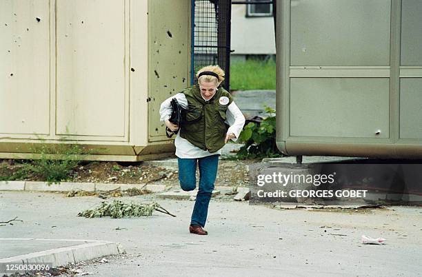 Woman wearing a bullet-proof vest runs for cover to escape shots during fighting in a Sarajevo suburb, on June 02, 1992.