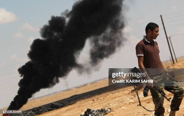 National Transitional Council fighter walks past a plume of black smoke at the frontline in Bani Walid, southeast of the capital Tripoli on October...