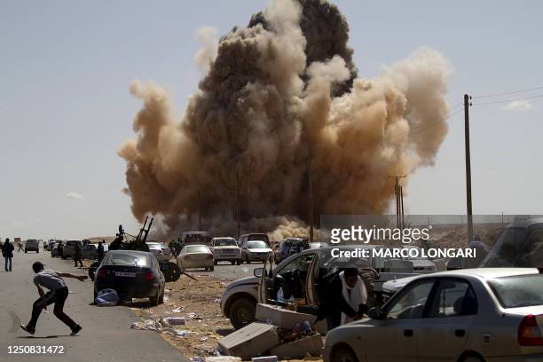 Libyan rebel fighters take cover as a bomb dropped by an airforce fighter jet explodes near a checkpoint on the outskirts of the oil town of Ras...