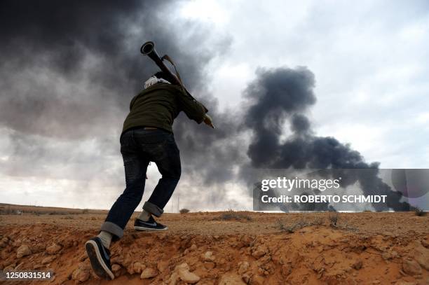 Libyan rebel fighter scarmbles from a ditch as he carries a rocket propelled grenade to reach the battle scene with forces loyal to leader Moamer...