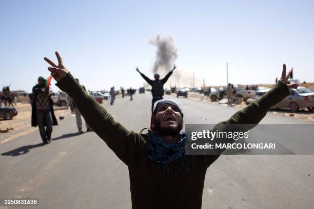 Libyan rebel fighters flash the victory sign as they look at an airforce fighter jet flying overhead after dropping a bomb near a checkpoint on the...