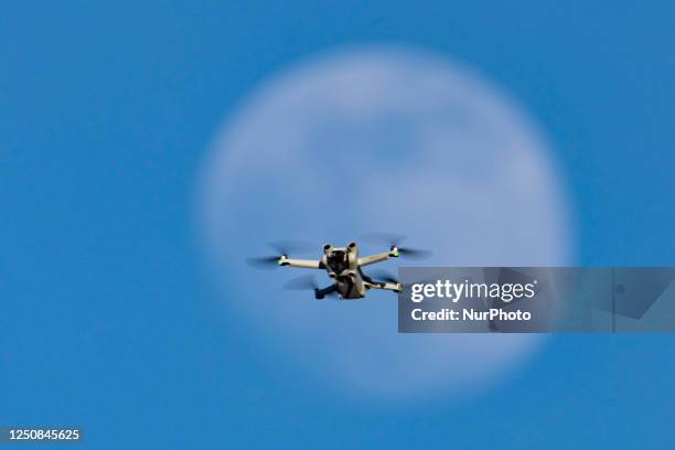 Pro consumer illustration of an Unmanned Aerial Vehicle UAV or quadcopter drone as seen flying and hovering in front of the moon during the day. The...