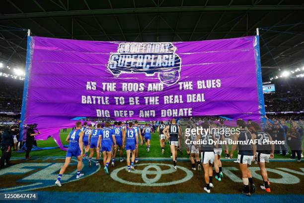 Players from both teams enter through a joint banner during the 2023 AFL Round 04 match between the North Melbourne Kangaroos and the Carlton Blues...