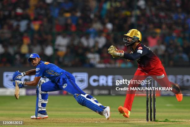 Mumbai Indians' Tilak Varma plays a shot as Royal Challengers Bangalore's wicketkeeper Dinesh Karthik tries to stop the ball during the Indian...