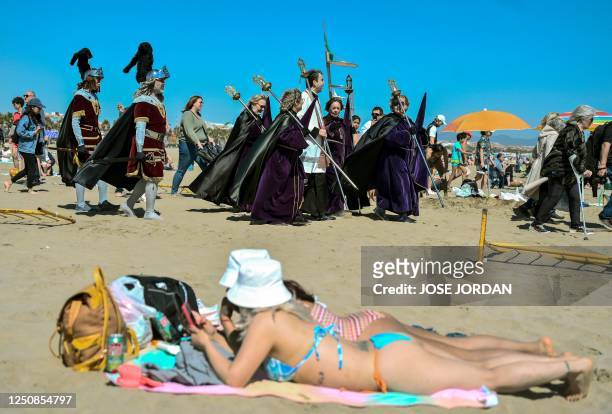 Priest surrounded by female penitents of "Cristo Salvador" brotherhood walk past sunbathers lying in the sun during the Good Friday procession...