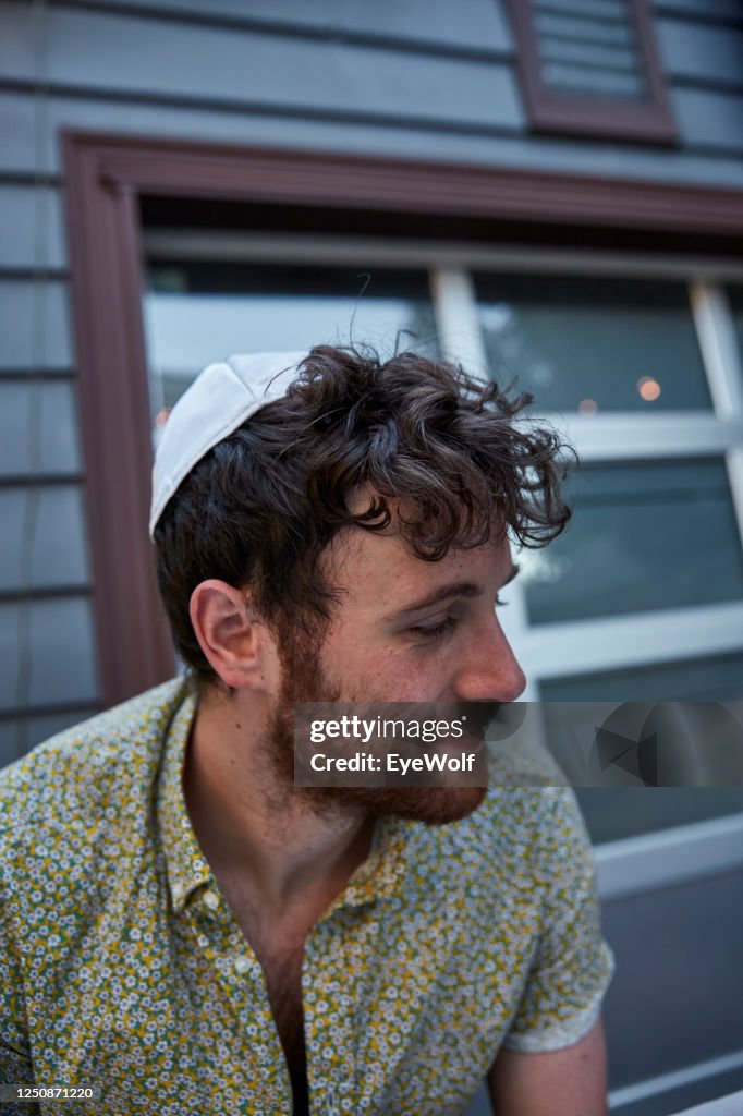 A young Jewish man sitting at a table outside wearing a Yamika, looking off camera.