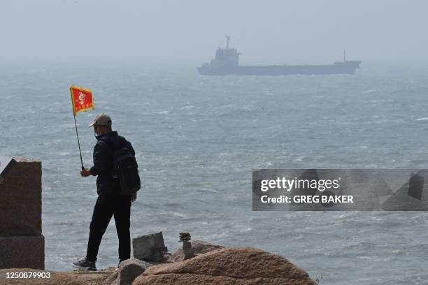 Man walks with a flag as a ship passes by behind him on Pingtan island, the closest point to Taiwan, in Chinas southeast Fujian province on April 8,...