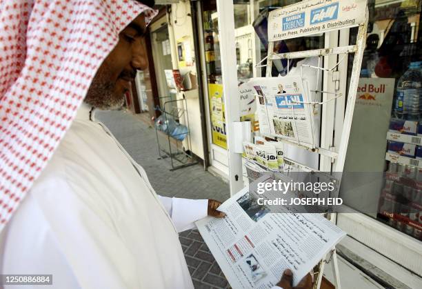 Bahraini man reads a newspaper while standing in front of a street newspaper stand in central Manama on March 21, 2011 as Bahrain's news agency...