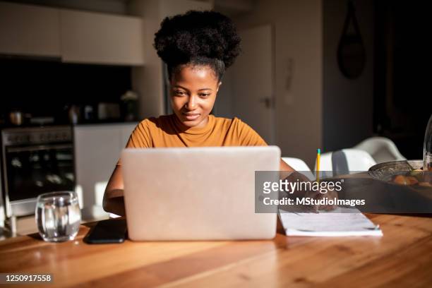 junge frau liest vom computer und macht sich notizen an ihrem notizbuch - woman portrait kitchen laptop stock-fotos und bilder