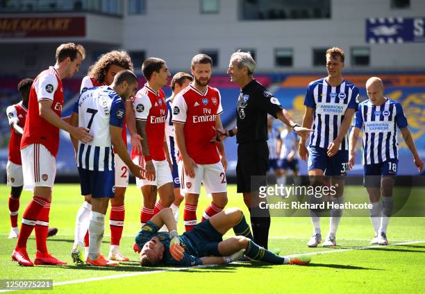 Referee Martin Atkinson speaks to Hector Bellerin and Shkodran Mustafi of Arsenal as Bernd Leno of Arsenal goes down injured as Neal Maupay of...