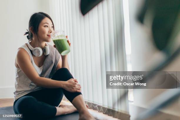 young asian woman drinking green smoothie after yoga - benessere foto e immagini stock