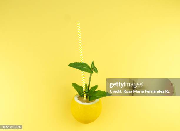 lemon fruit with one stripe straw and mint leaf  stuck in it over yellow background. summer drink concept. lemonade for summer heat. ingredient for drink - cocktail umbrella foto e immagini stock