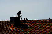 Silhouette of a chimney sweeper on top of a roof