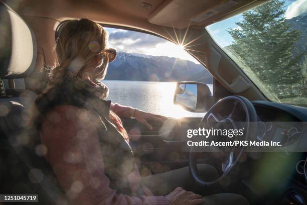 portrait of a woman watching the sun rise across a lake from her vehicle - car sun stock pictures, royalty-free photos & images