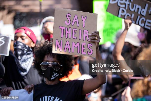 An African American protester wears a mask that say "I Can't Breathe" and holds a sign that says, "Say Their Names" as they perform a peaceful...