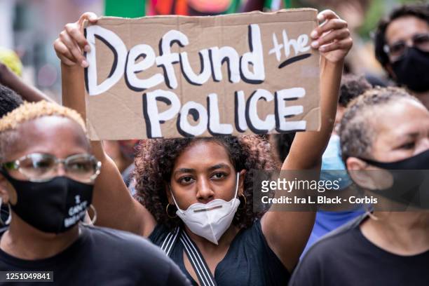 An African American protester wears a mask and holds a homemade sign that says, "Defund the Police" as they perform a peaceful protest walk across...