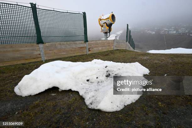 April 2023, North Rhine-Westphalia, Winterberg: A snow cannon stands on a ski slope on last patches of snow, the season is over. Despite cold...