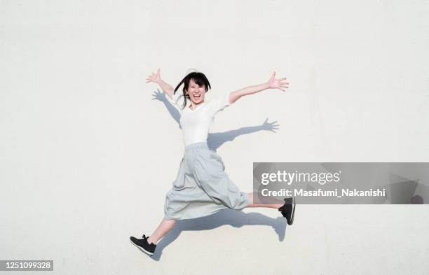 photo de femme asiatique sautant avec le sourire devant le mur blanc - sauter photos et images de collection